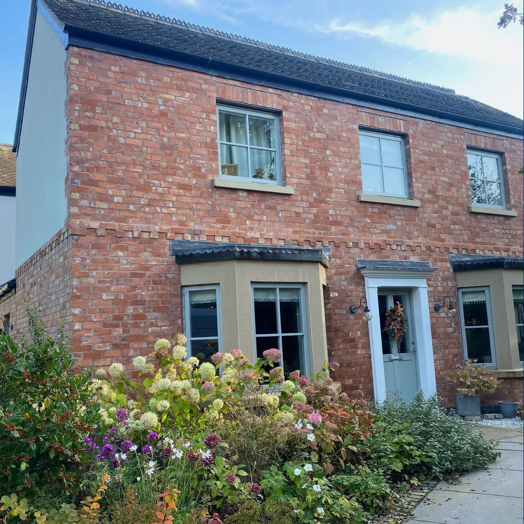 Finished red-brick conversion with two bay windows, grey front door and established garden